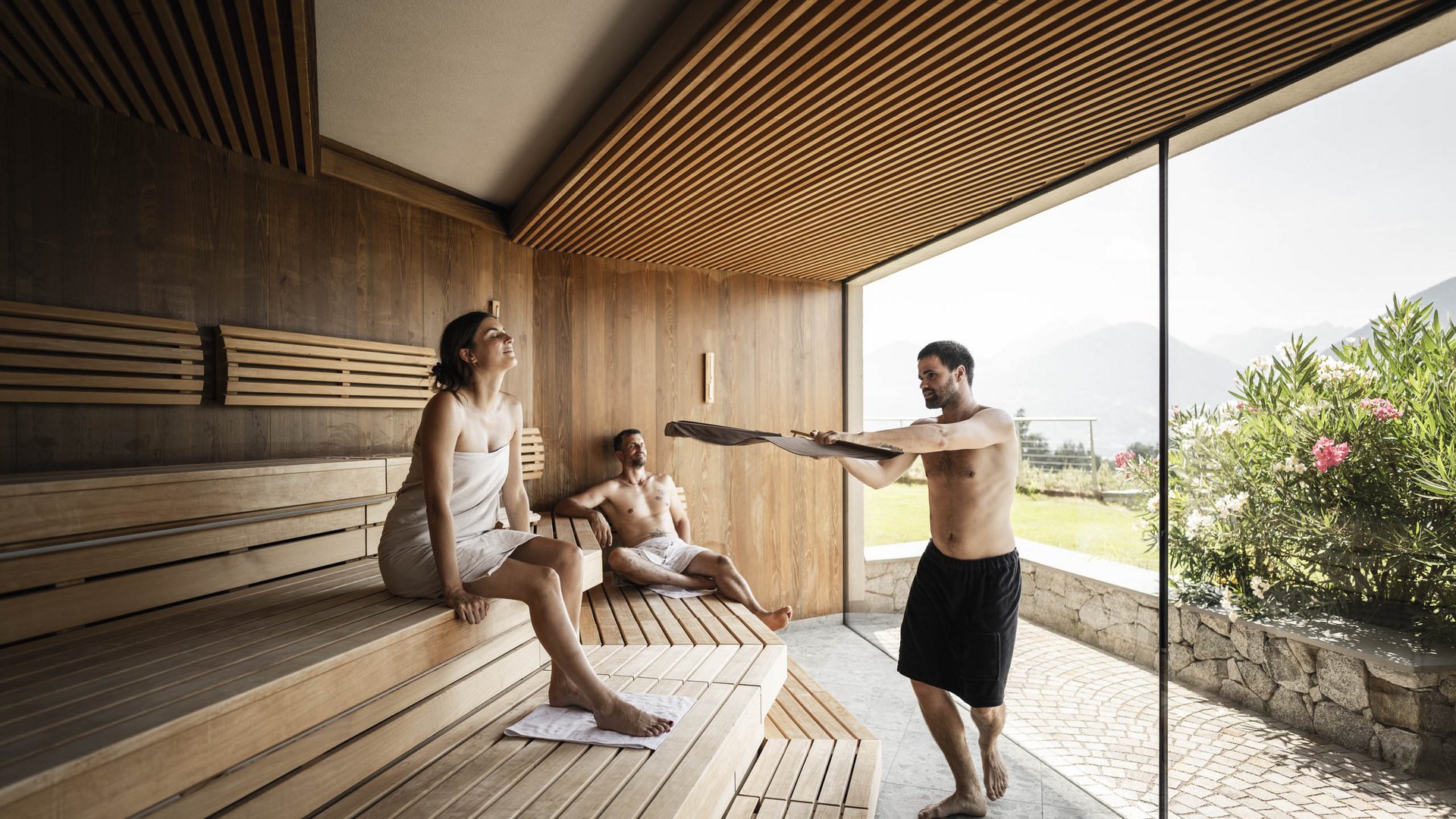 Schenna Resort People relaxing in a sauna with wooden walls and large window overlooking garden