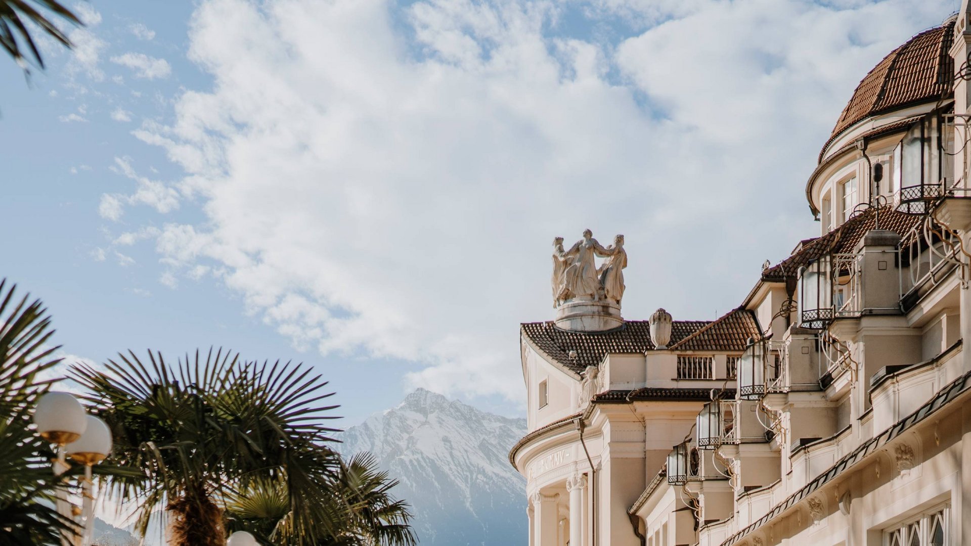 Schenna Resort Historic building with statues overlooking snow-covered mountain and palm trees